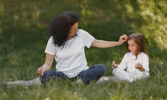Mother and daughter bonding through yoga outdoors in a serene grassy field.