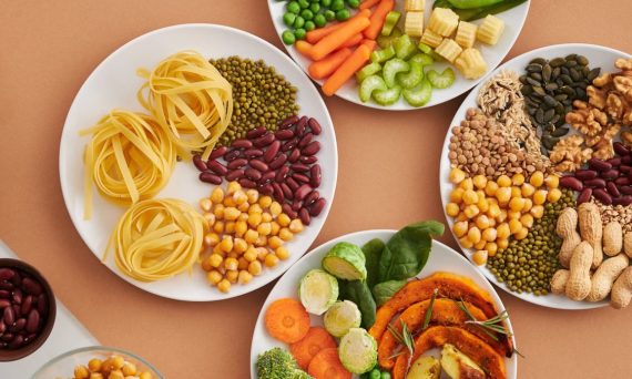 A vibrant mix of legumes, vegetables, nuts, and pasta arranged on white plates showcasing a balanced, healthy diet.